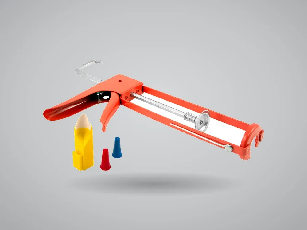 A dripless caulking gun with its plunger drawn back, beside spare nozzles