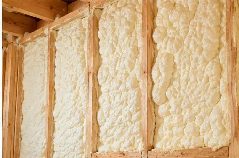 Cream-colored spray foam expanded to fill the cavities between wall studs