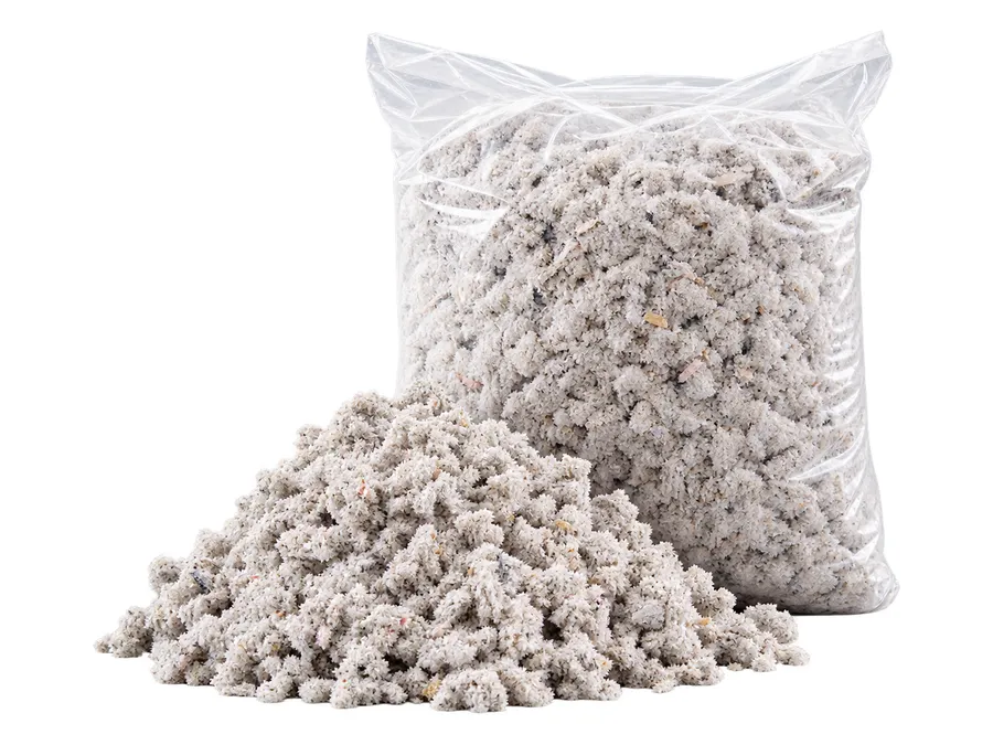 A clear bag of blown-in cellulose insulation beside a loose pile of the gray shredded fiber