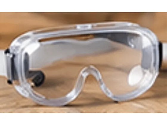 Clear sealed safety goggles with an adjustable strap, resting on a workbench
